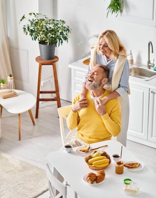 A man seated in a chair tenderly holds a woman, embodying love and togetherness in a cozy home setting.